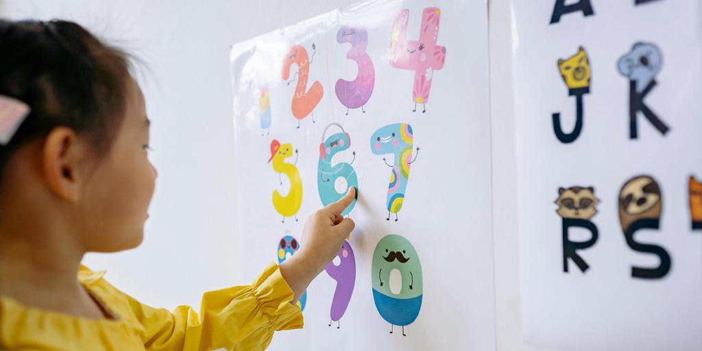 a young girl points at a poster with numbers zero to nine
