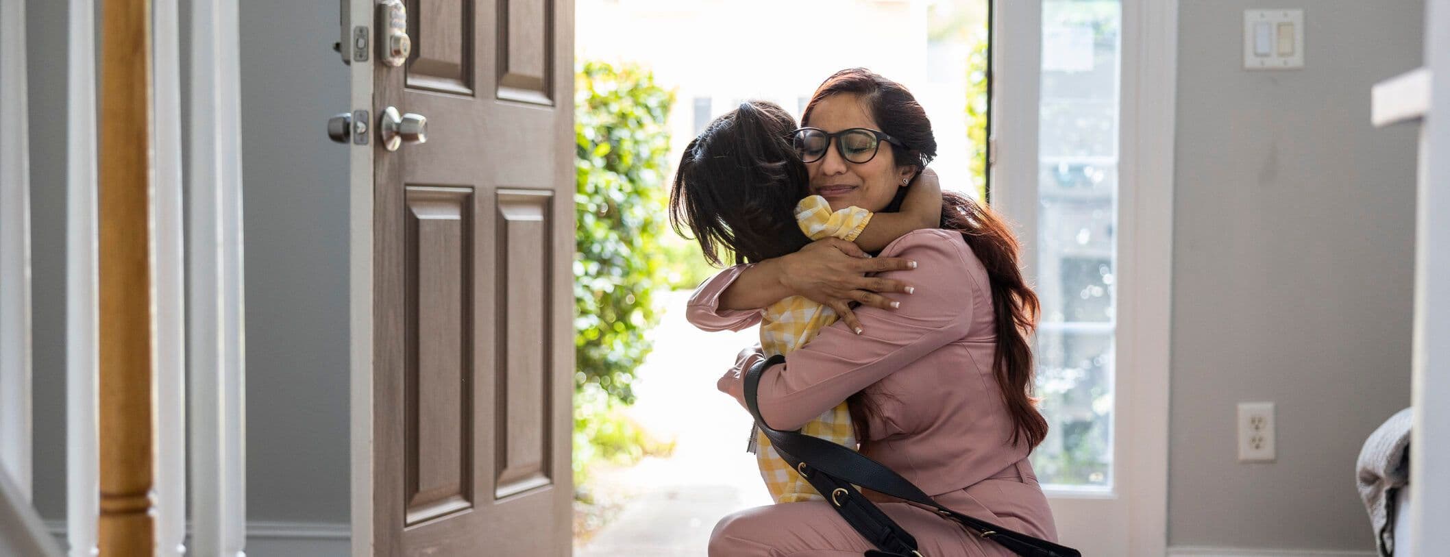 Toddler girl embracing mother in doorway as she gets home from work
