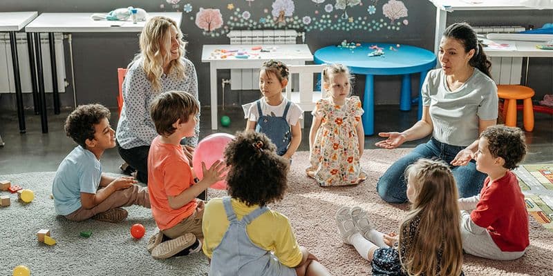 a group of preschoolers sit on the carpet with their teachers