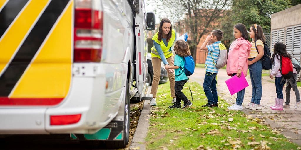 a teacher helps students board the school bus