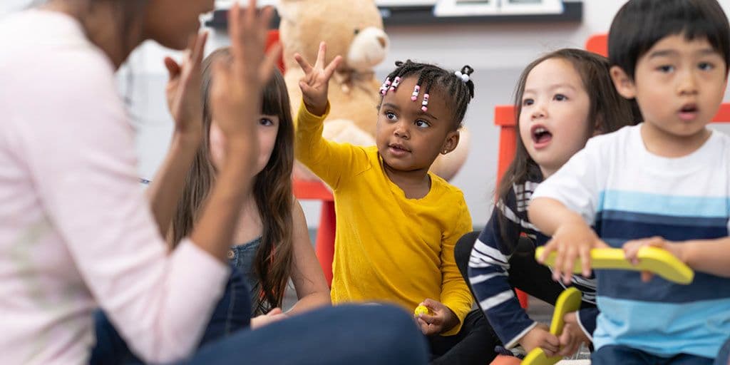 a young child raises her hand in daycare