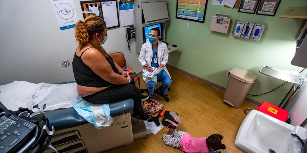 a woman listens to her doctor while her daughter plays nearby