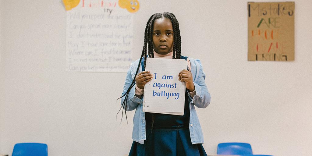 a young girl stands holding a sign that reads "I am against bullying"