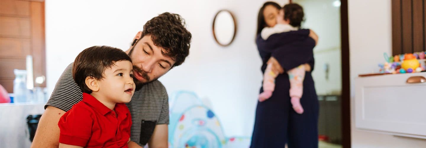 a father holds his young son, while a mother stands in the background