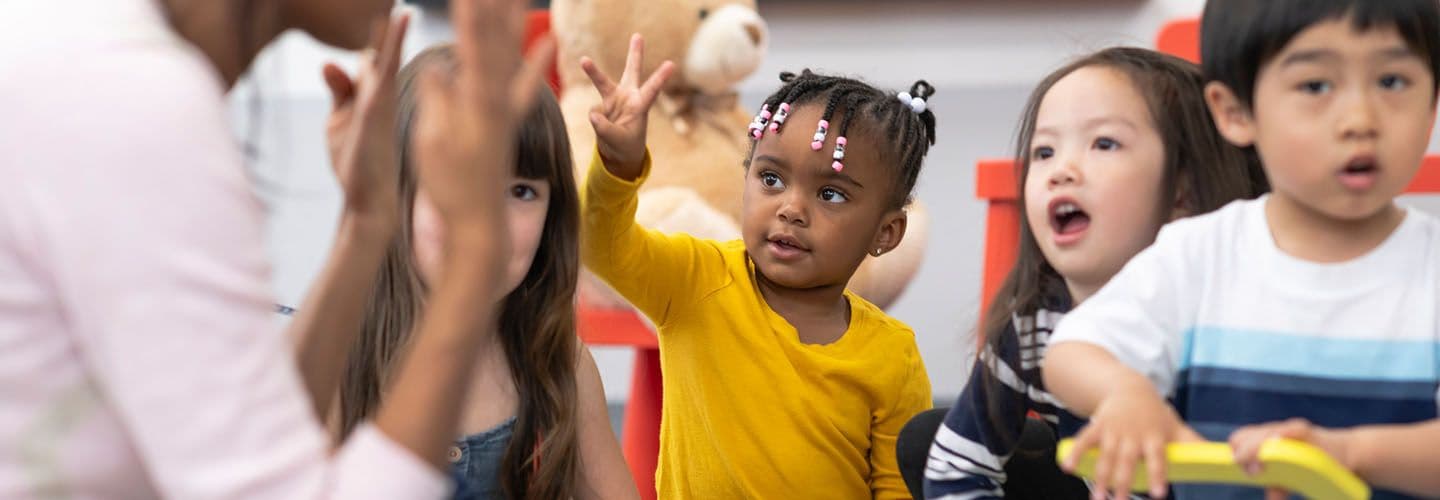 a young child raises her hand in daycare
